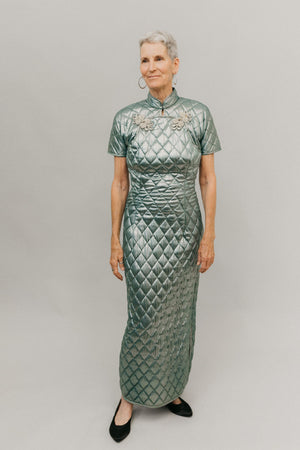 Photo of woman in ankle length 122 Hong Kong Cheongsam.  Fabric is a quilted shinny light green with ornate metallic frog closures.