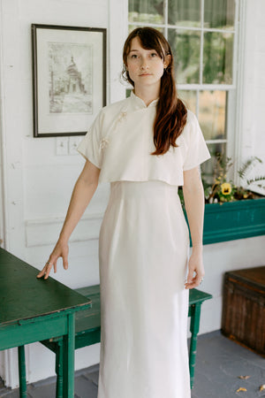 Woman wearing a white cheongsam standing on a porch.