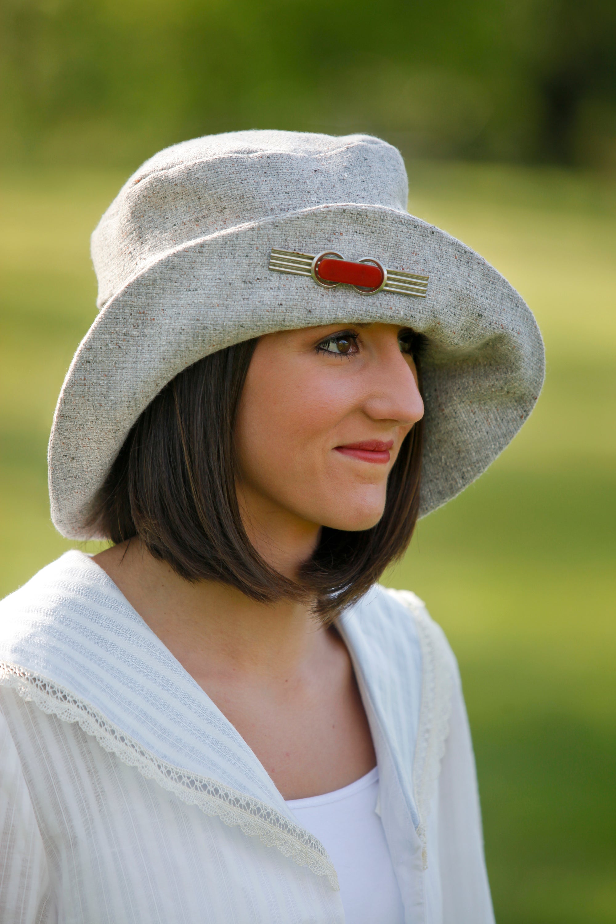 Young brunette white women wearing red lipstick. Wearing the #269 Metropolitan Hat in gray with a red brooch on the brim of the hat.