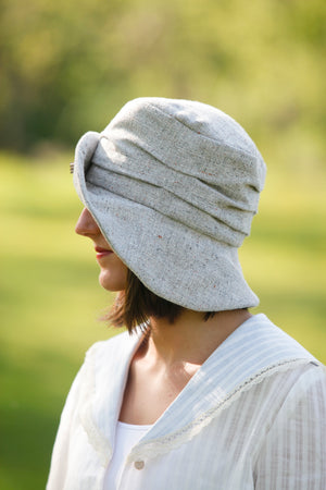 the left side view of young brunette white woman in a white blouse wearing the Metropolitan hat.