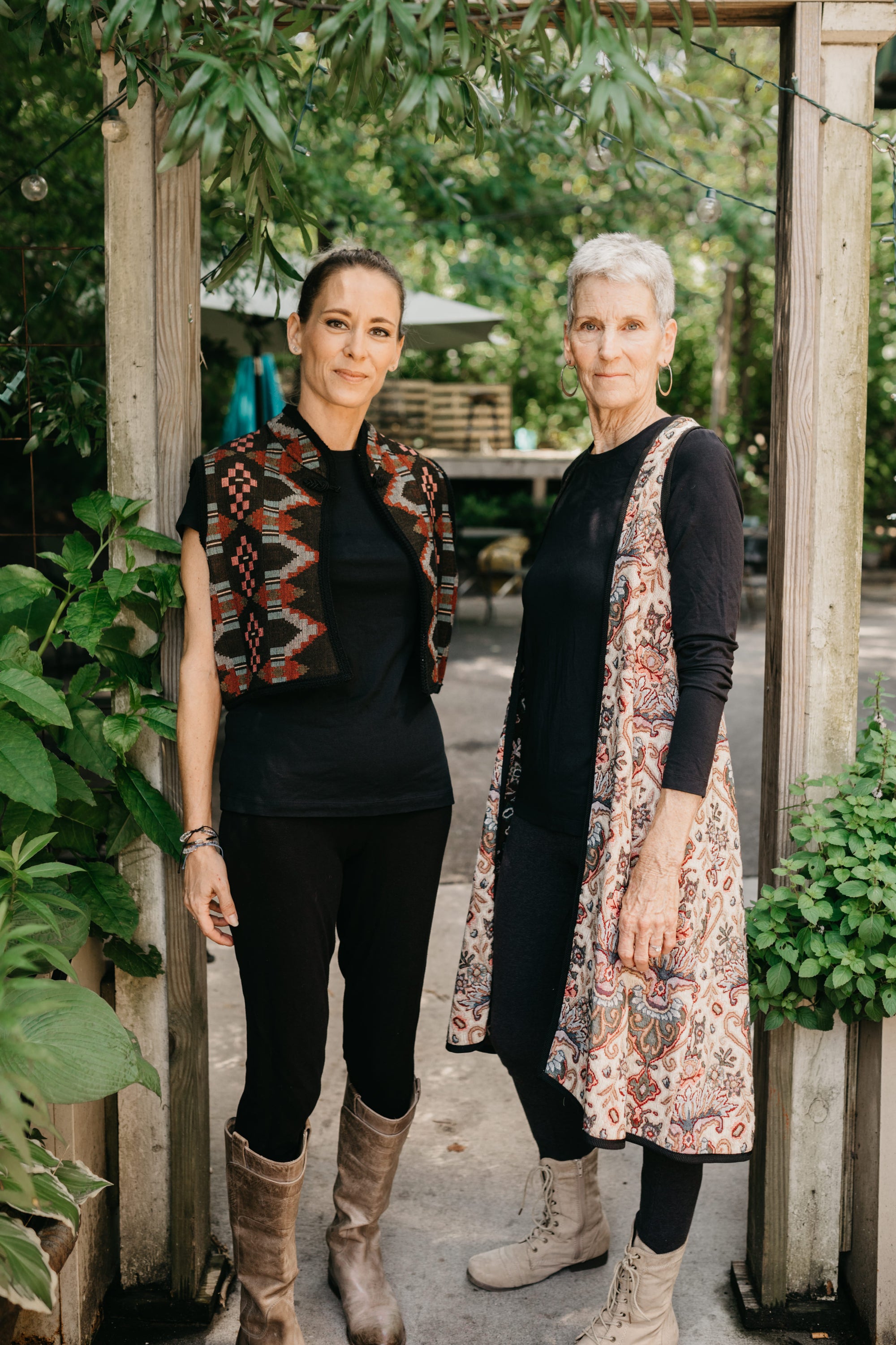 Photo of two women standing outdoors side by side.  Woman on left wears Short Greek Vest and woman on right wears Long Greek Vest.