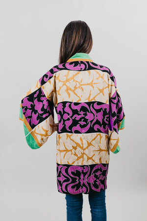 Asian woman wearing a purple, black, green, and gold printed Haori - back view with white back ground.