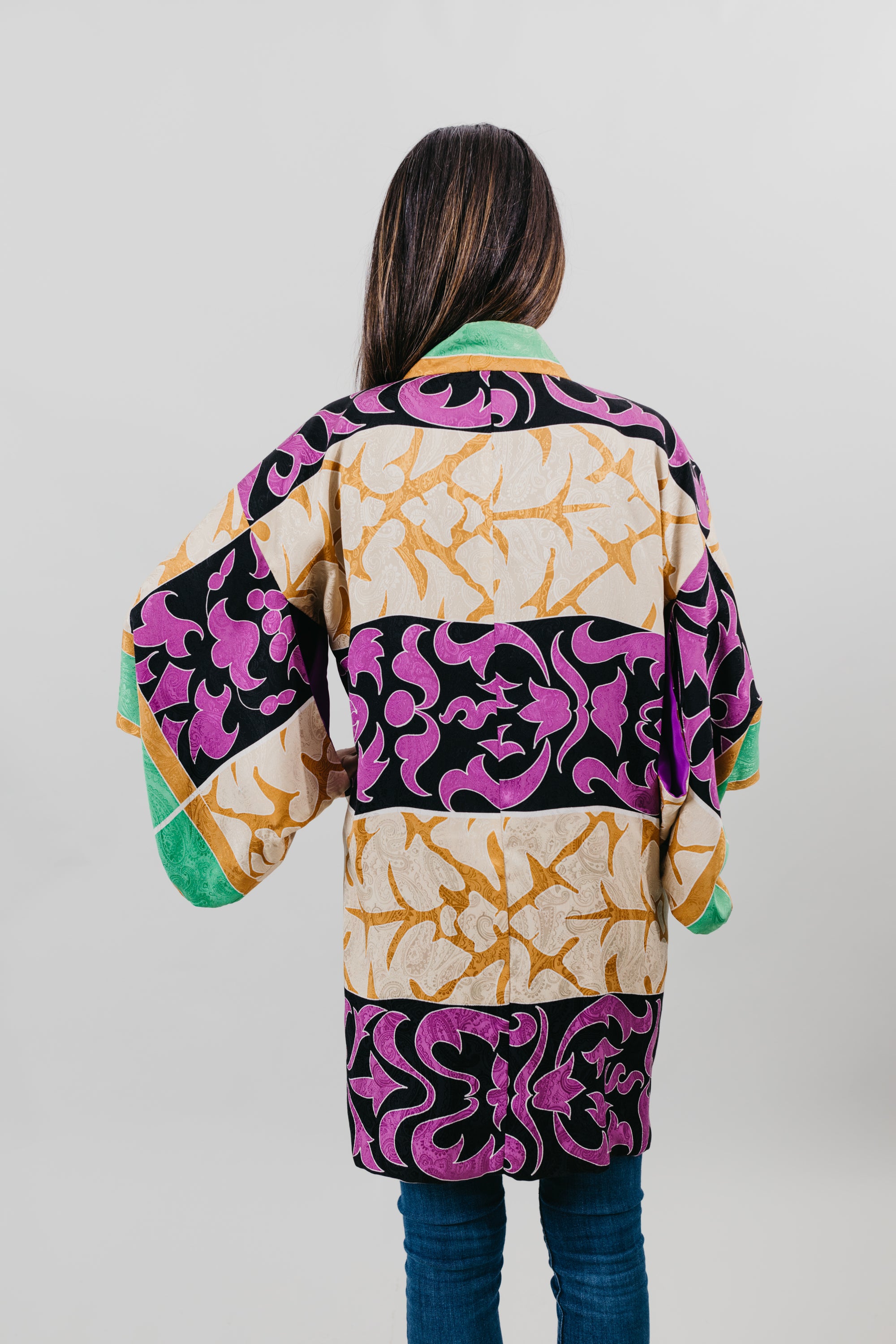 Asian woman wearing a purple, black, green, and gold printed Haori - back view with white background