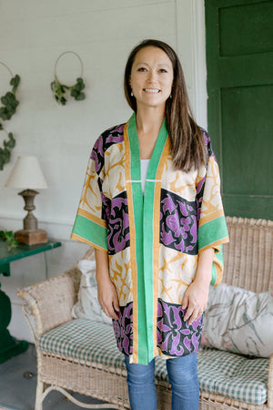Asian woman wearing a purple, black, green, and gold printed Haori standing on a porch.