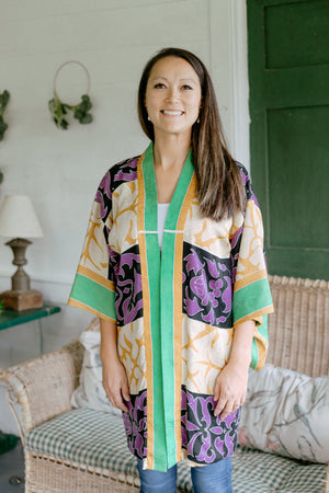 Asian woman wearing a purple, black, green, and gold printed Haori standing on a porch.