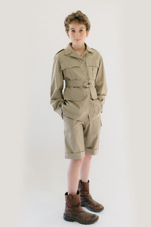 Boy wearing 130 Australian Bush Outfit  Jacket and shorts.  Standing in front of white backdrop with hands in shorts pockets.