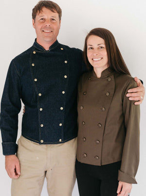 Man and woman standing together wearing a navy and brown Belgian Military Chef's Coats, respectively.  White backdrop.