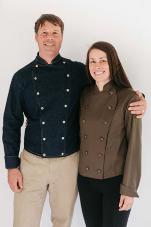 Man and woman standing together wearing a navy and brown Belgian Military Chef's Coats, respectively.  White backdrop.
