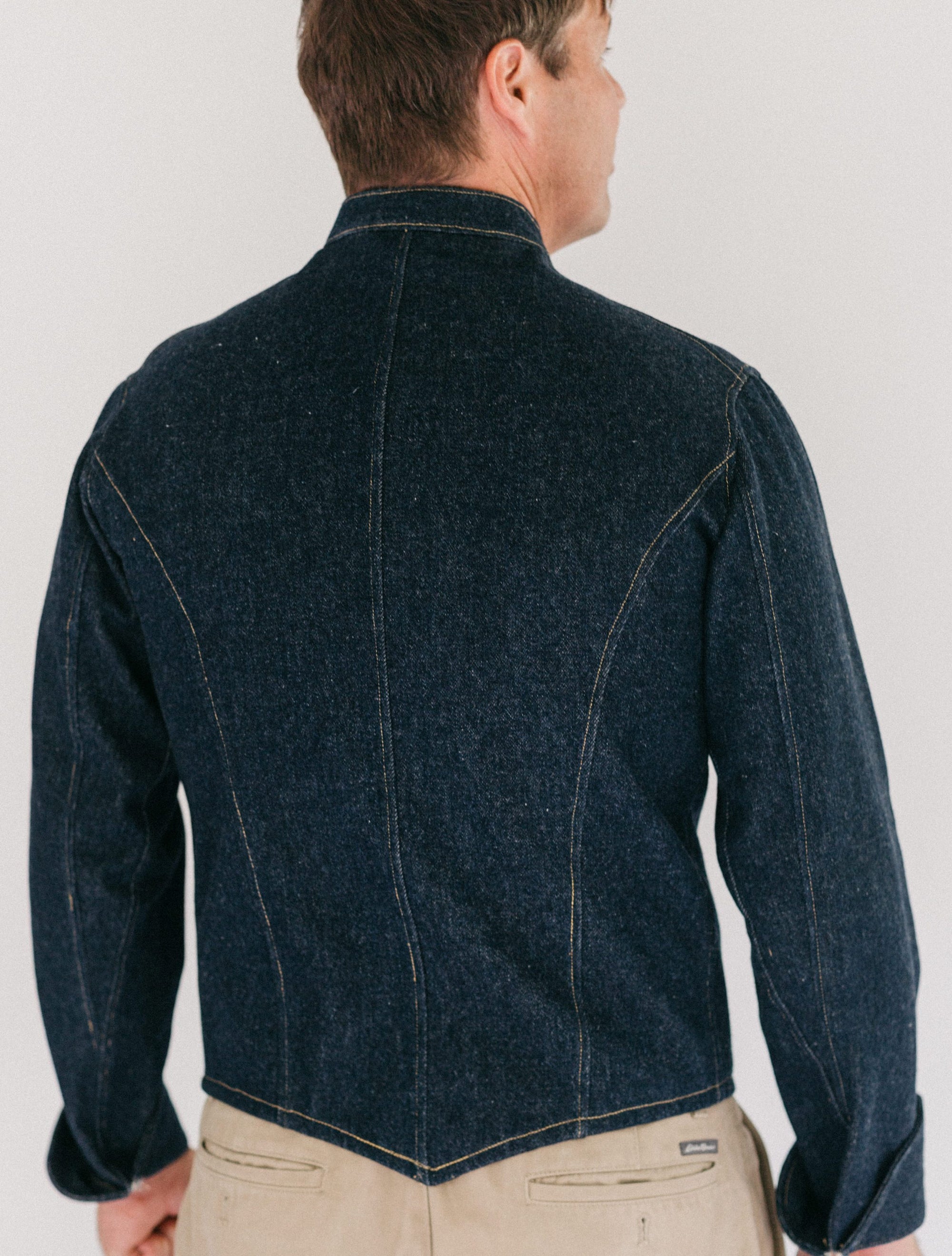 Back of Man wearing a dark denim Belgian military chef's coat. white background.