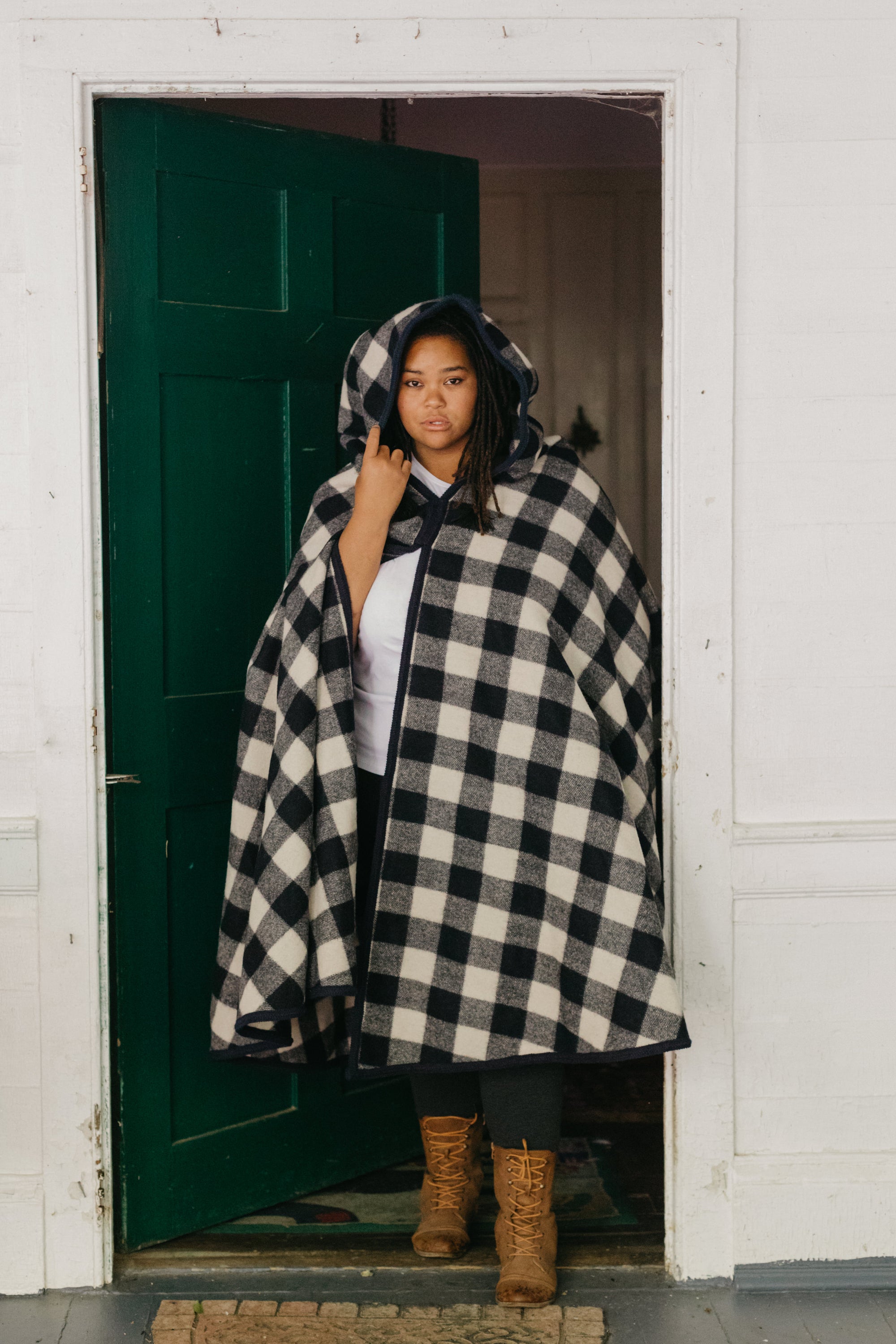 Black woman standing in a door wearing a large black and white checked burnoose with the hood up.