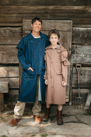 Man and boy wearing Drovers coats standing outside of a wooden building