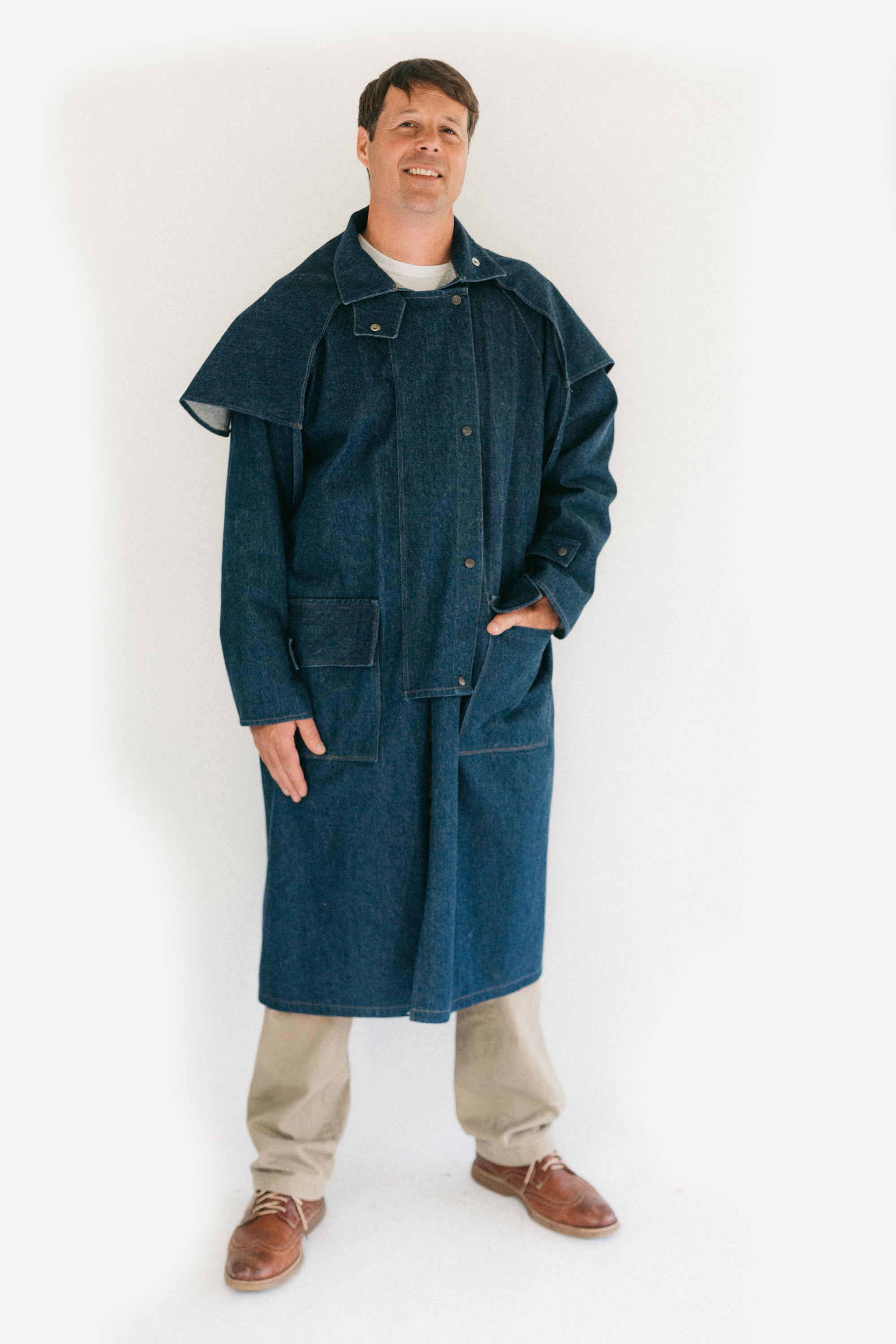 Man standing in front of a white screen wearing a dark blue Drover's Coat.