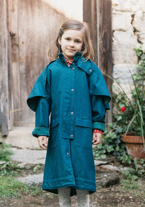 Young girl wearing a blue Australian Drovers Coat. standing out side in front of a wooden building.