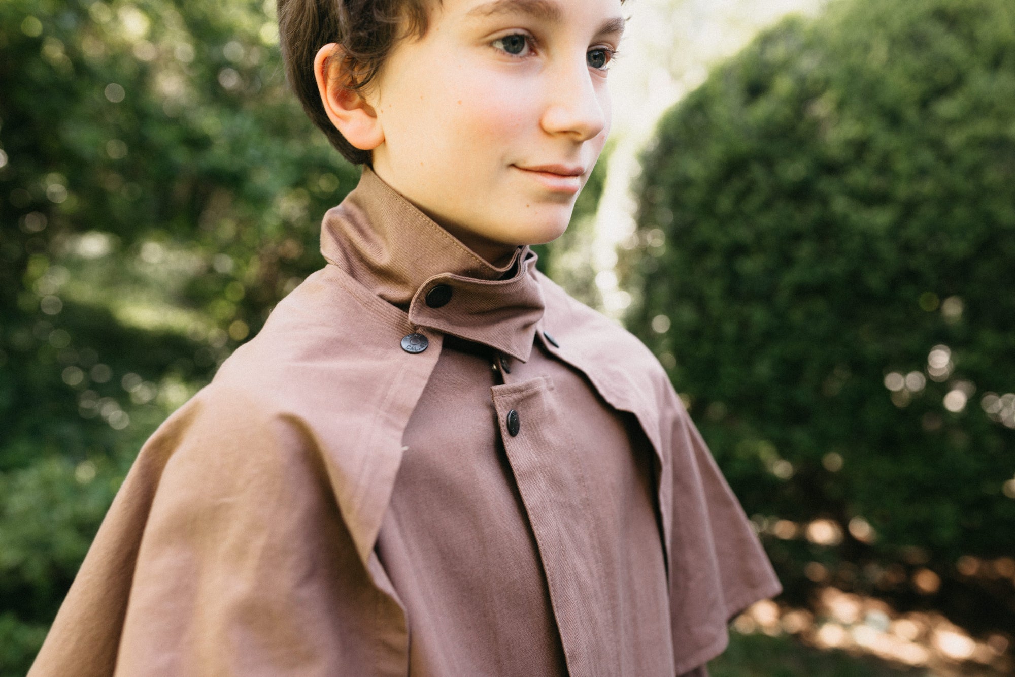 Close up of boy wearing brown Drovers coat with capelet. 