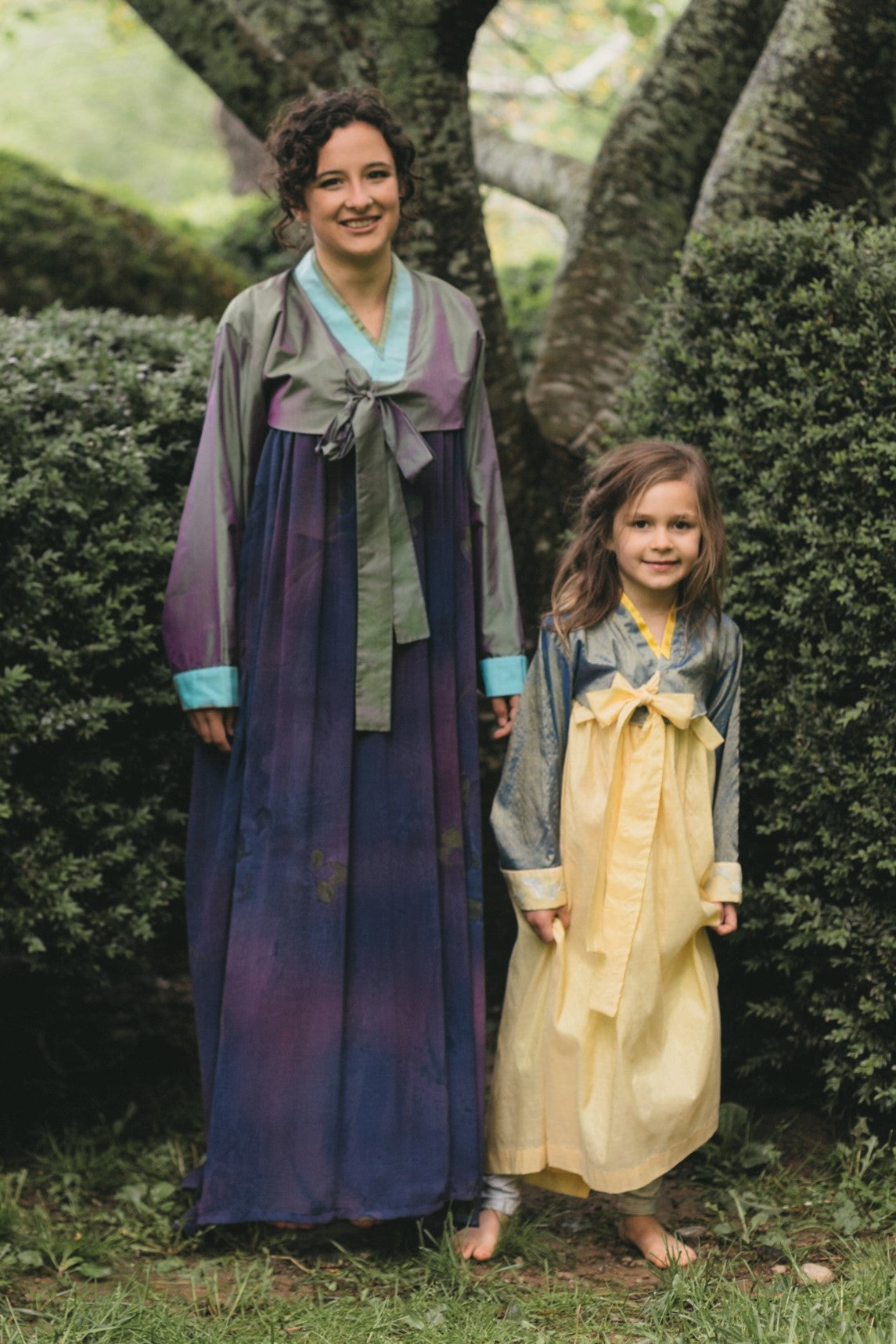 Photo of young woman and young girl standing side by side outdoors in the Han-Bok.  