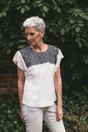 Older woman wearing Old Mexico Blouse outdoors in front of a brick wall with wisteria vines growing behind her.  