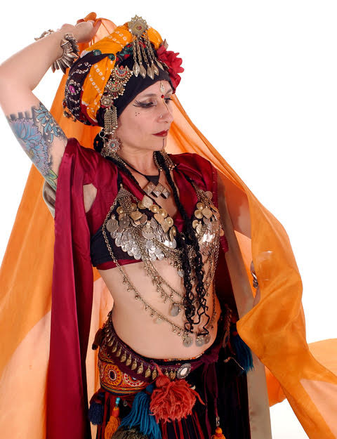 Belly dancer in coin bra and headdress and tassels and scarves.  Colors are orange and red.