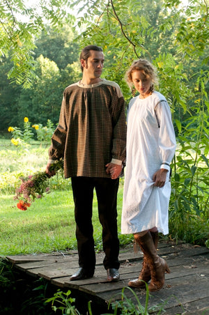 Young white man holding flowers and woman standing on a bridge surrounded by greenery wearing the 148 Black Forest Smock.