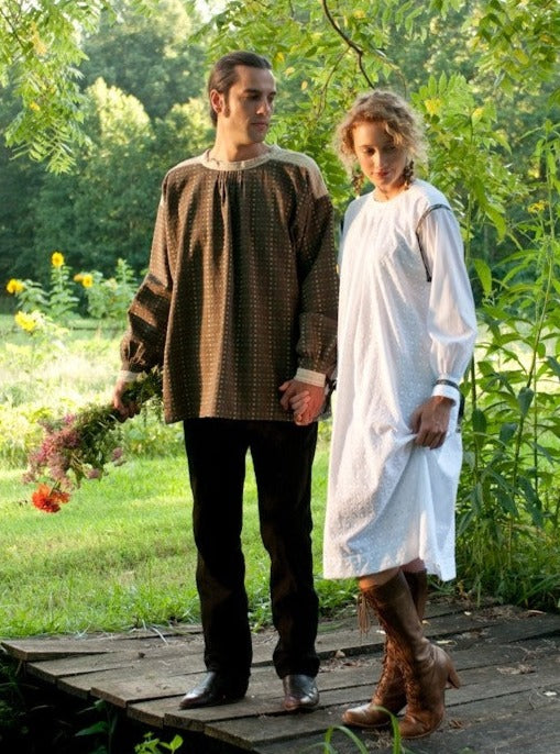 Young white man holding flowers and woman standing on a bridge surrounded by greenery wearing the 148 Black Forest Smock.