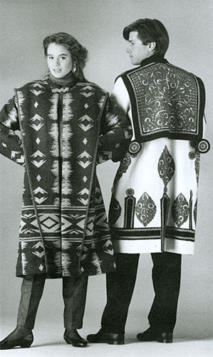 Black and white photo of an man and woman standing side by side in two versions of the Szur.  Woman is facing forward and wears view B (contemporary) man's back is facing the camera and is wearing view A (traditional) szur.