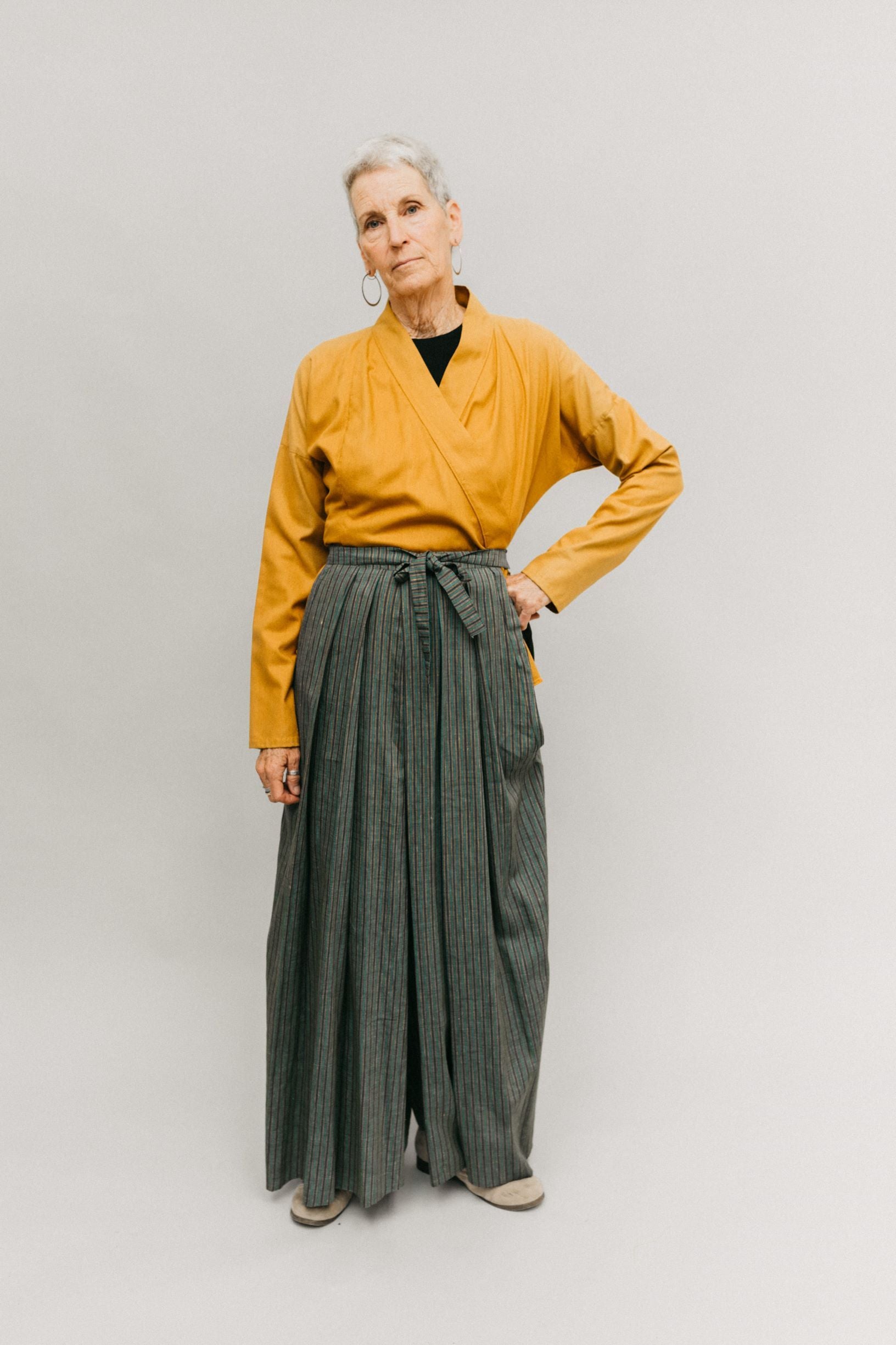 Photo of woman wearing Hakama pants.  Standing in front of a studio backdrop.  Left hand on hip.