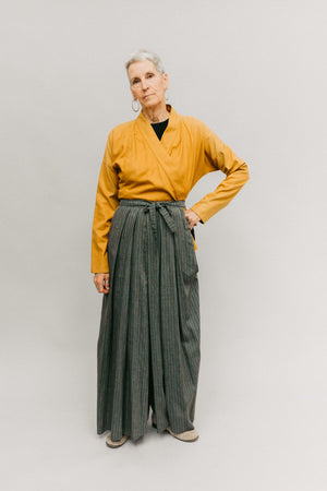 Photo of woman wearing Hakama pants.  Standing in front of a studio backdrop.  Left hand on hip.
