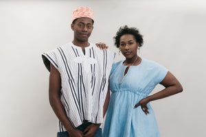 An African American young man and women standing in front of a white studio backdrop wearing the Ghanaian Smock. 