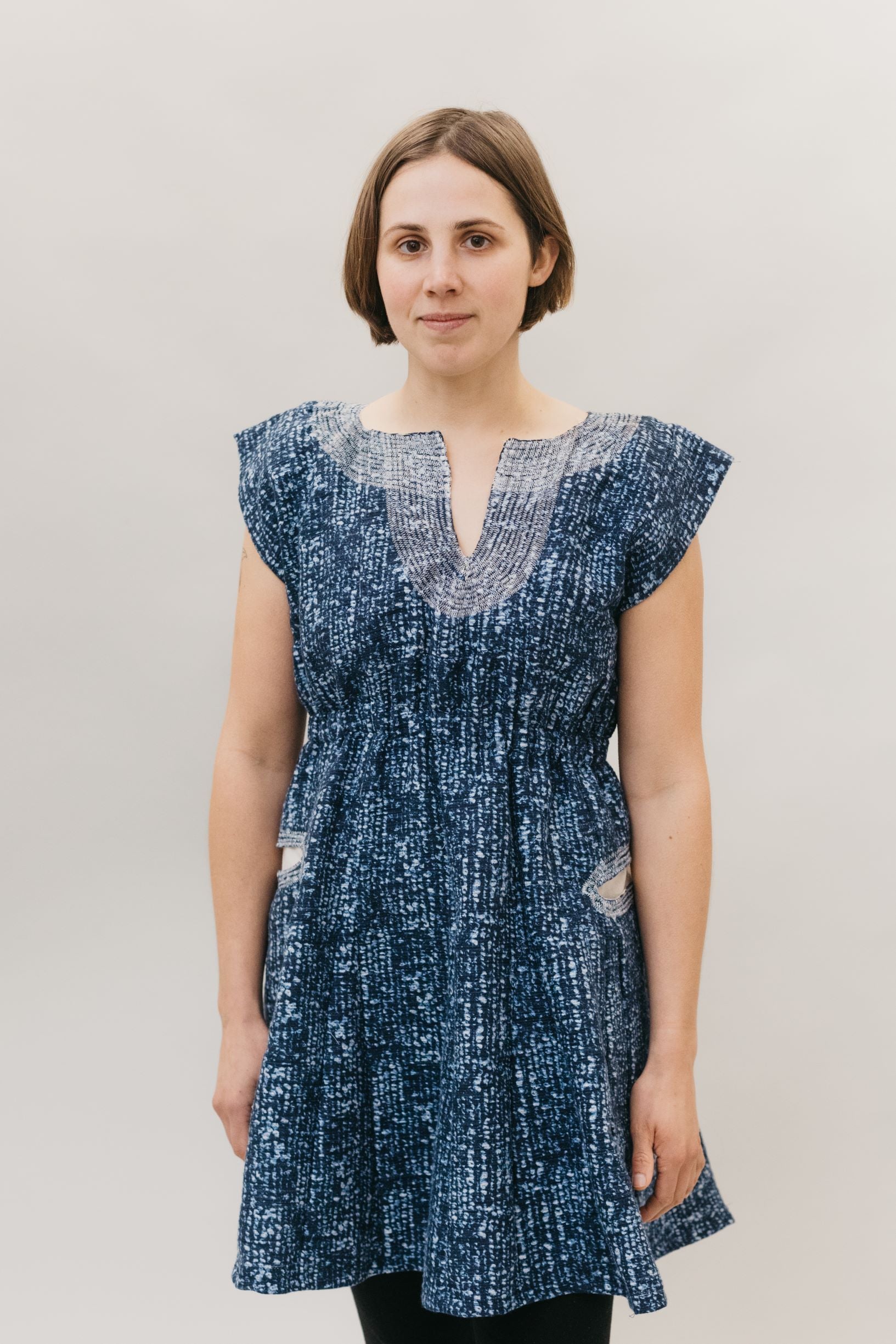 young brunette white woman standing in front of a white studio backdrop wearing the Ghanaian Smock.