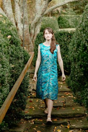 Woman walking down stone steps outside in a sleeveless teal brocade muumuu.