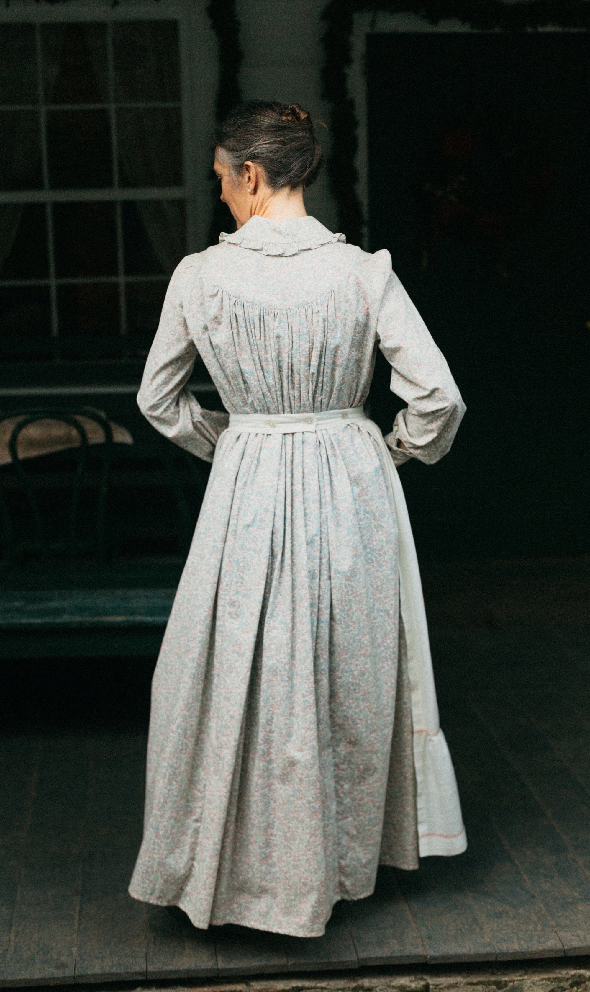 Photo of back view of prairie dress and apron waistband.  Model stands outside with hands in front pocket.