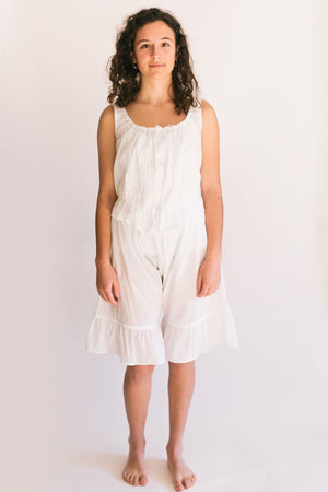 Photo of young woman standing in front of a white studio backdrop wearing camisole and drawers.