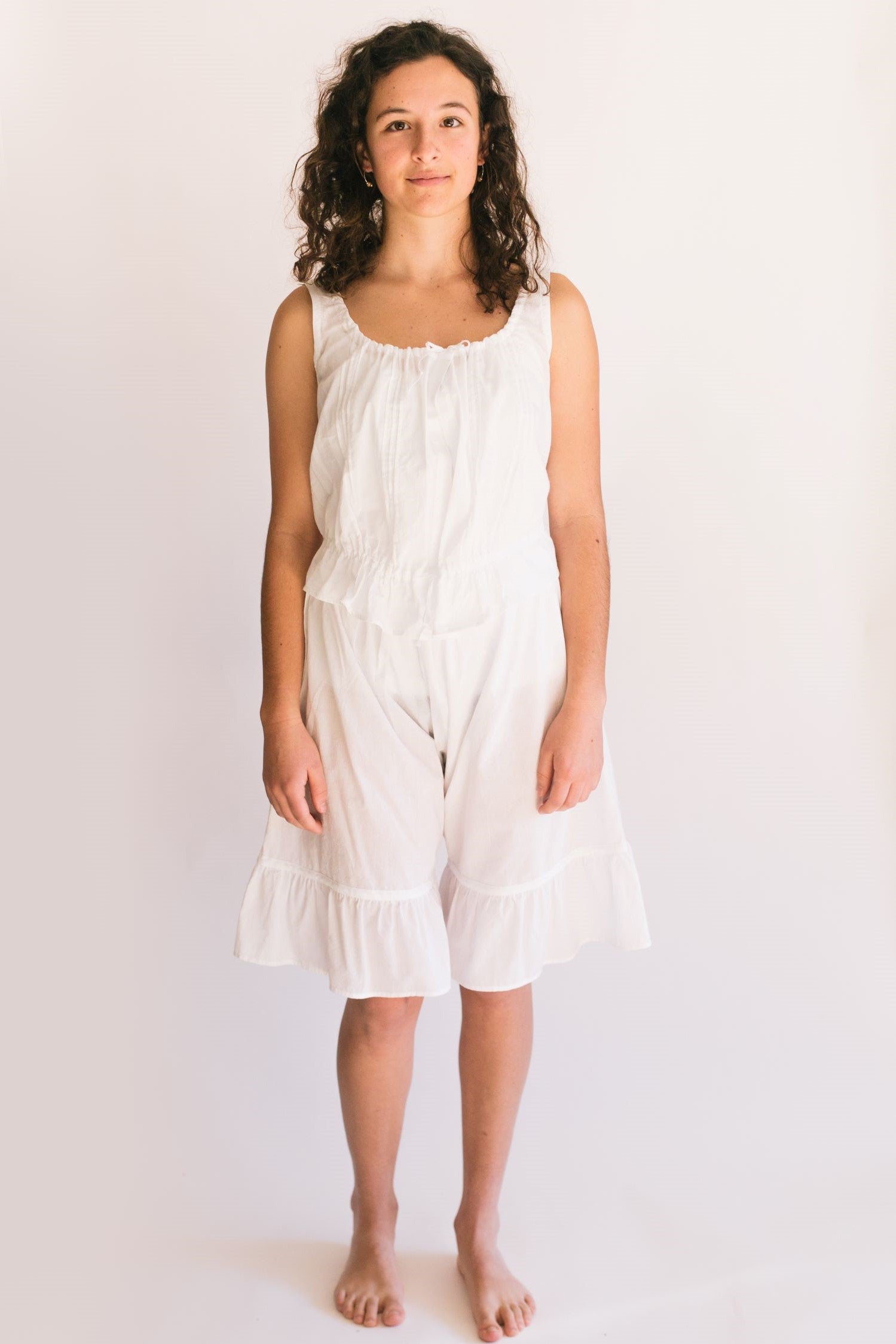 Photo of young woman standing in front of a white studio backdrop wearing camisole and drawers.