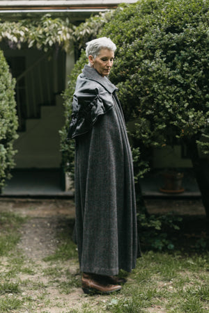 Older white woman with short gray hair standing surrounded by greenery turned to the side wearing 207 Kinsale Cloak with hood down over shoulders.