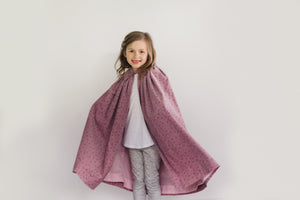 Smiling small girl standing in front of a white studio backdrop wearing 208 Kinsale Cloak for Young Maidens arms extended to either side to display the voluminous cloak.