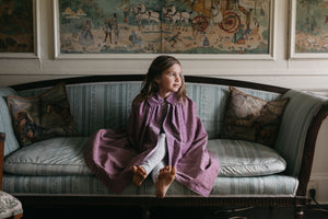 Little girl sitting on a sofa in a room wearing 208 Kinsale Cloak for young Maidens. 