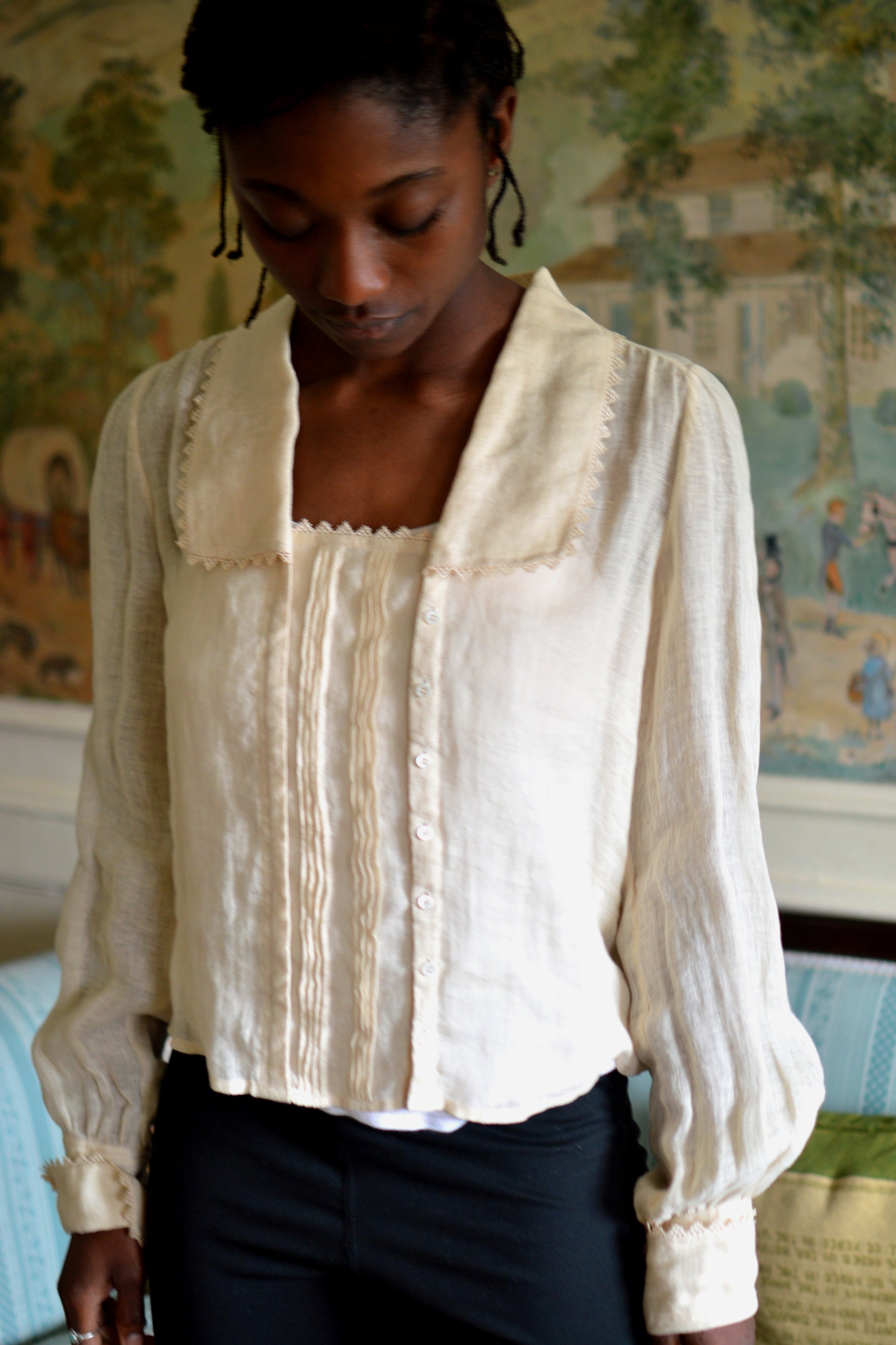 African woman standing in a room looking down wearing 210 Armistice Blouse., and black leggings. 