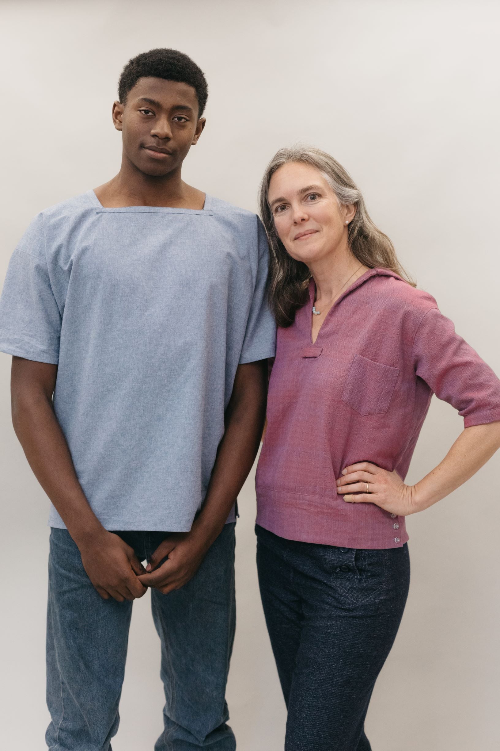 A young African American man and a white woman standing in front of a studio white backdrop wearing 211 Two middies, one with a square neck the other with a v-neck.
