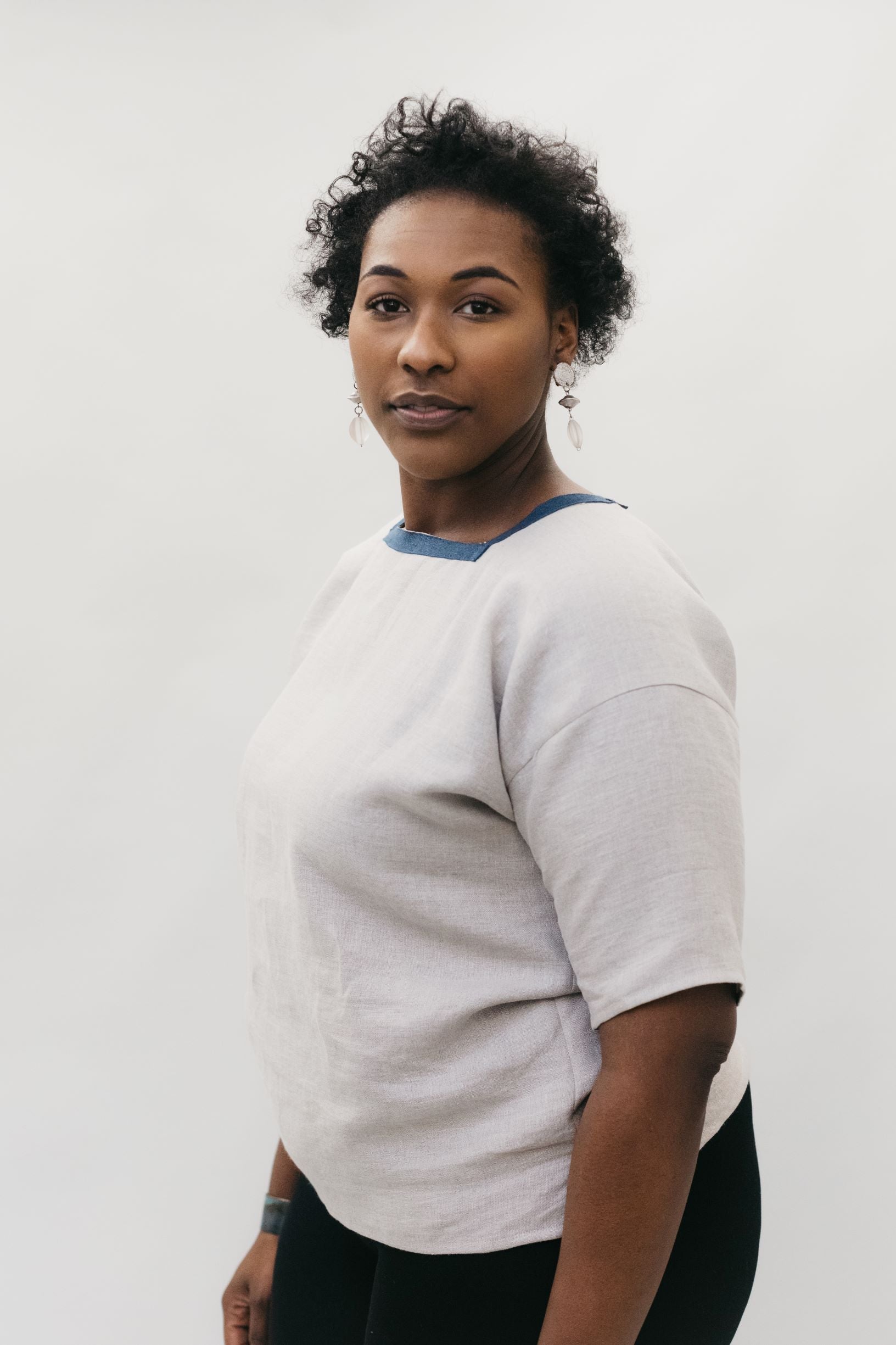 side view of African American woman wearing the square neck 211 Two Middies standing in front of a white studio backdrop. 