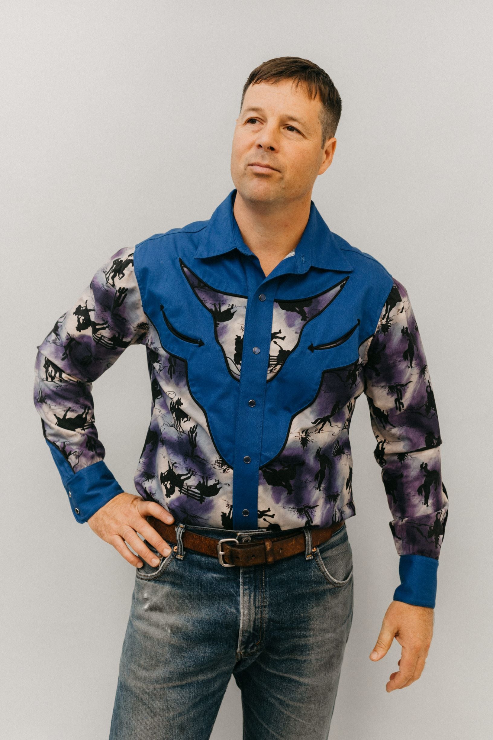 Man with hand on hip standing in front of a white studio backdrop wearing 212 Five Frontier Shirt View D with decorative bull's head yoke.