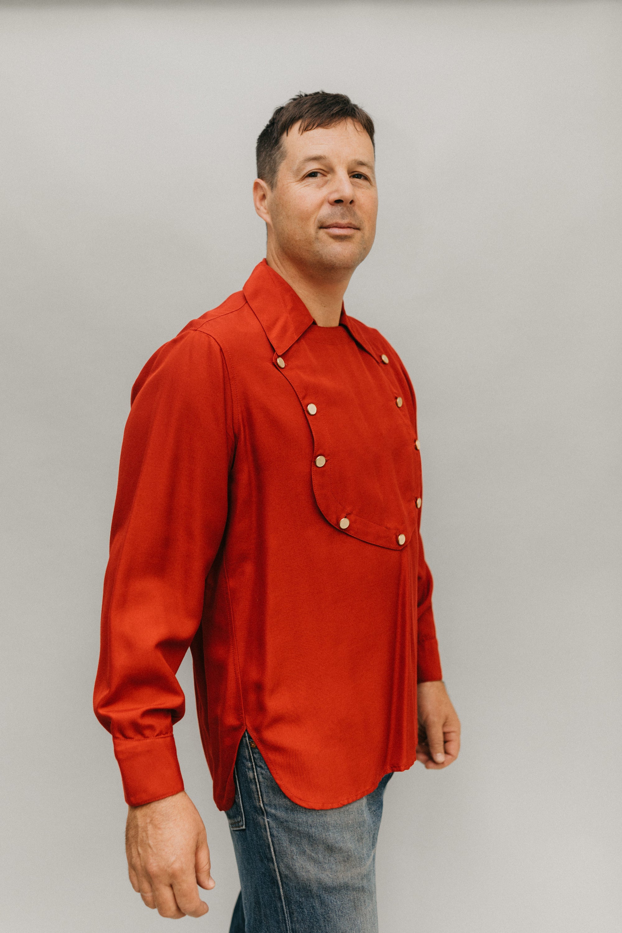 Man standing slightly turned to the side in front of a white studio backdrop wearing 212 Five Frontier Shirts View C with buttoned front bib.