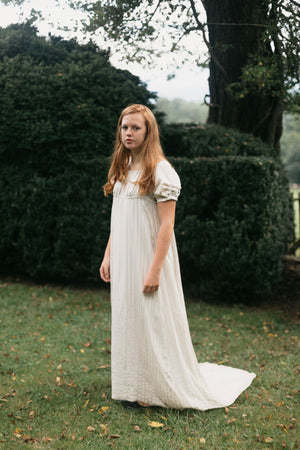 Red head young woman standing surrounded by greenery wearing 215 Empire Dress authentic version with a train. 