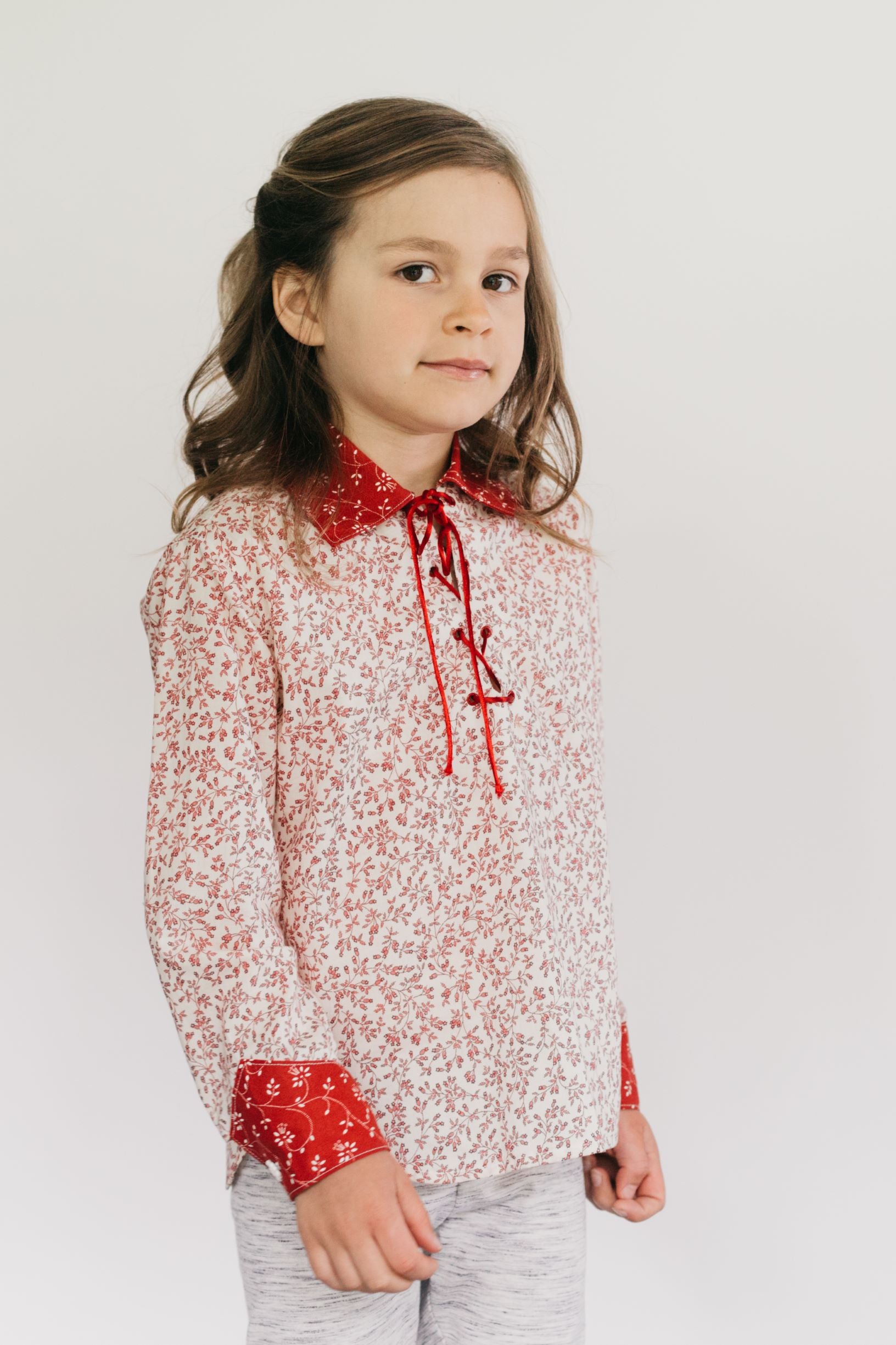 Small child with brunette hair standing in front of a white studio backdrop wearing 218 Child's Frontier Shirt, with lace up front, pointed collar with shaped cuffs. 