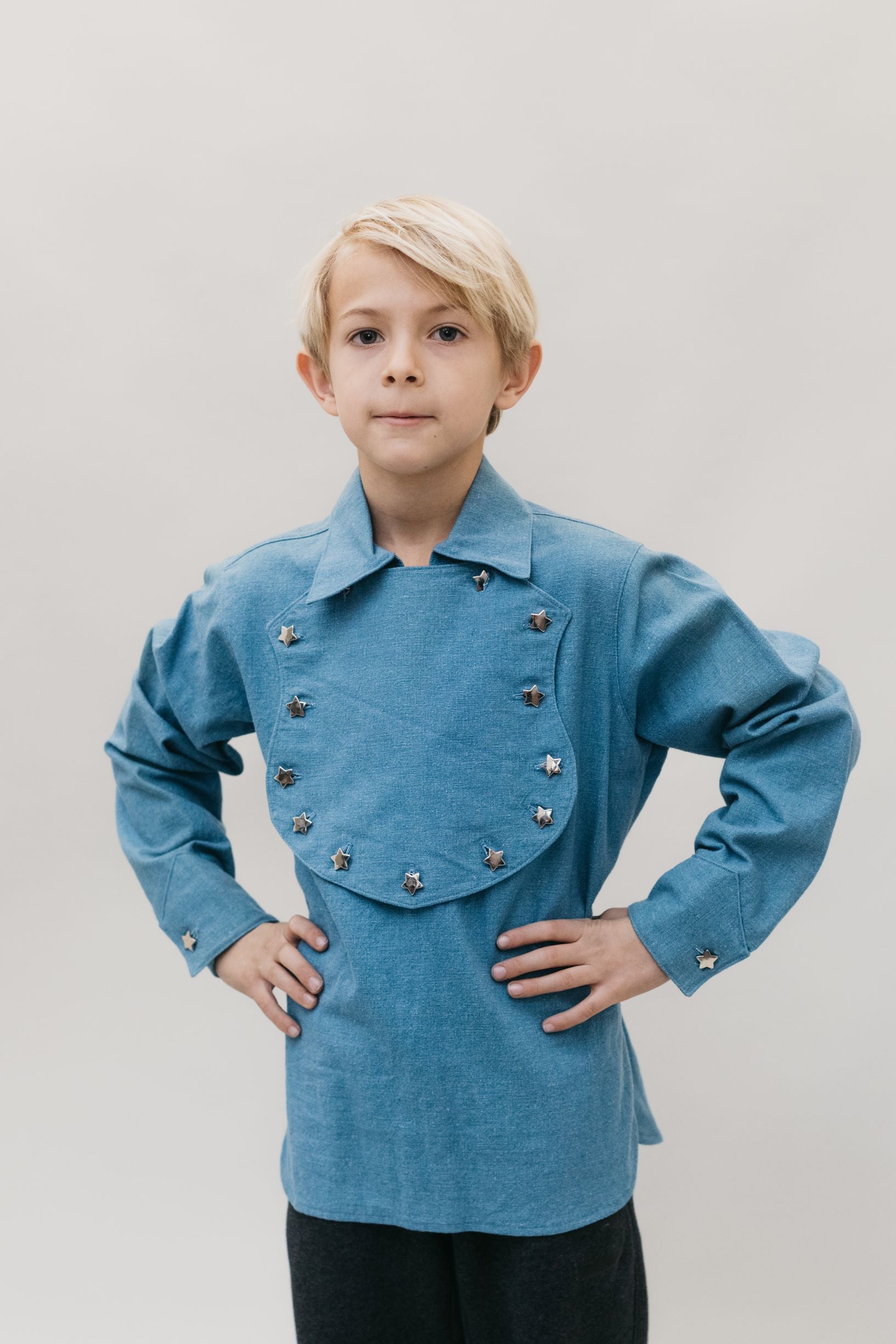 Small Blonde child with hands on his hips standing in front of a white studio backdrop, wearing 218 Child's Frontier Shirt View C Fireman's bib. 