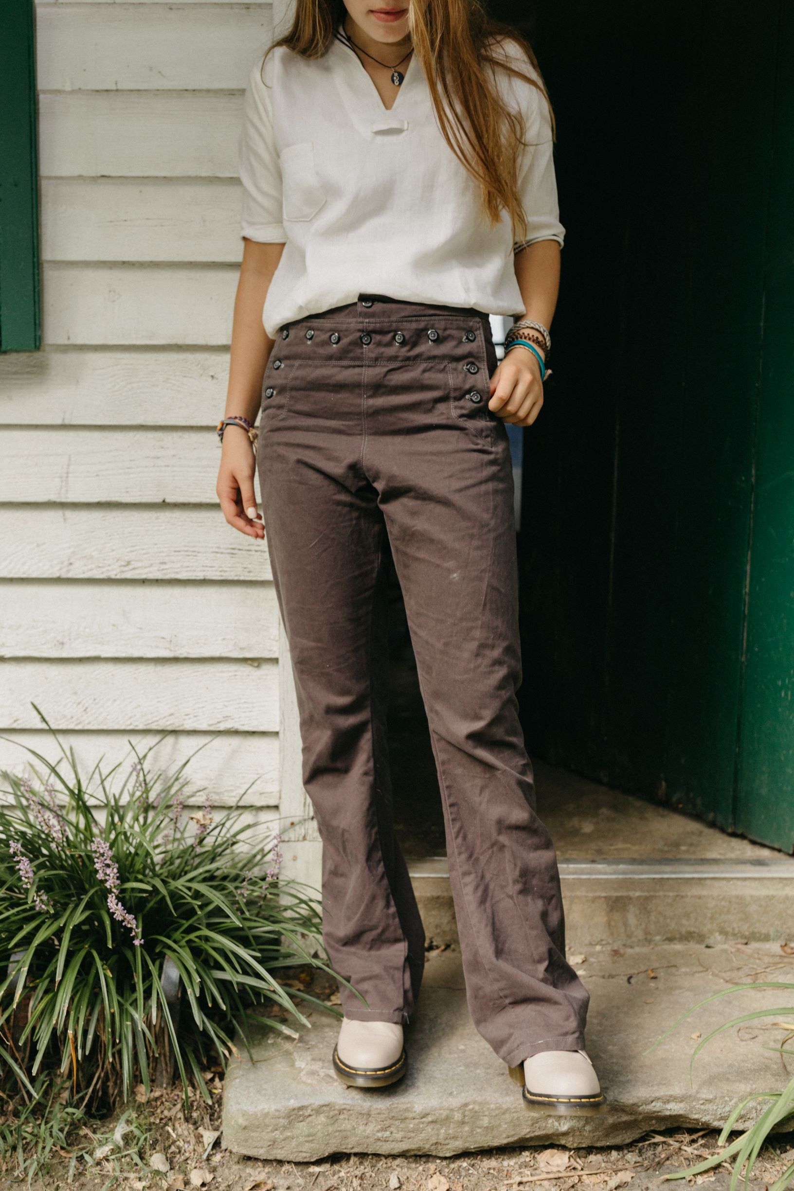 Young girl standing in front of a doorway wearing 229 Sailor Pants with 211 Two Middies, and beige shoes.