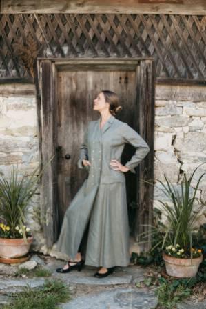 Woman standing in front of stone building knee bent with hands on hips looking to the left wearing 230 Model T Duster.