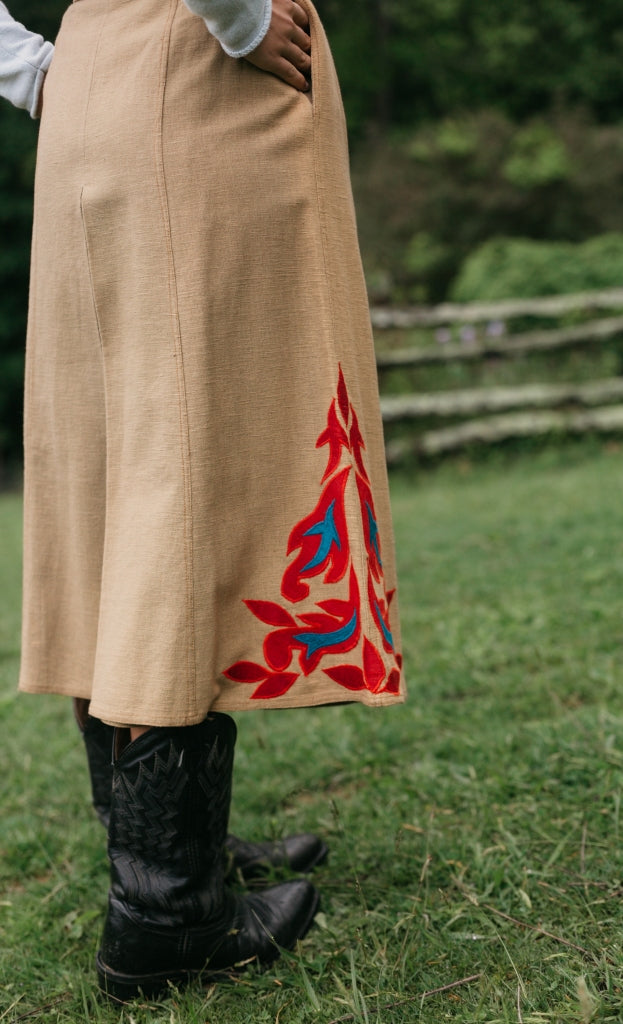 Close up back view of a woman wearing 231 Big Sky Riding Skirt and black boots surrounded by greenery.