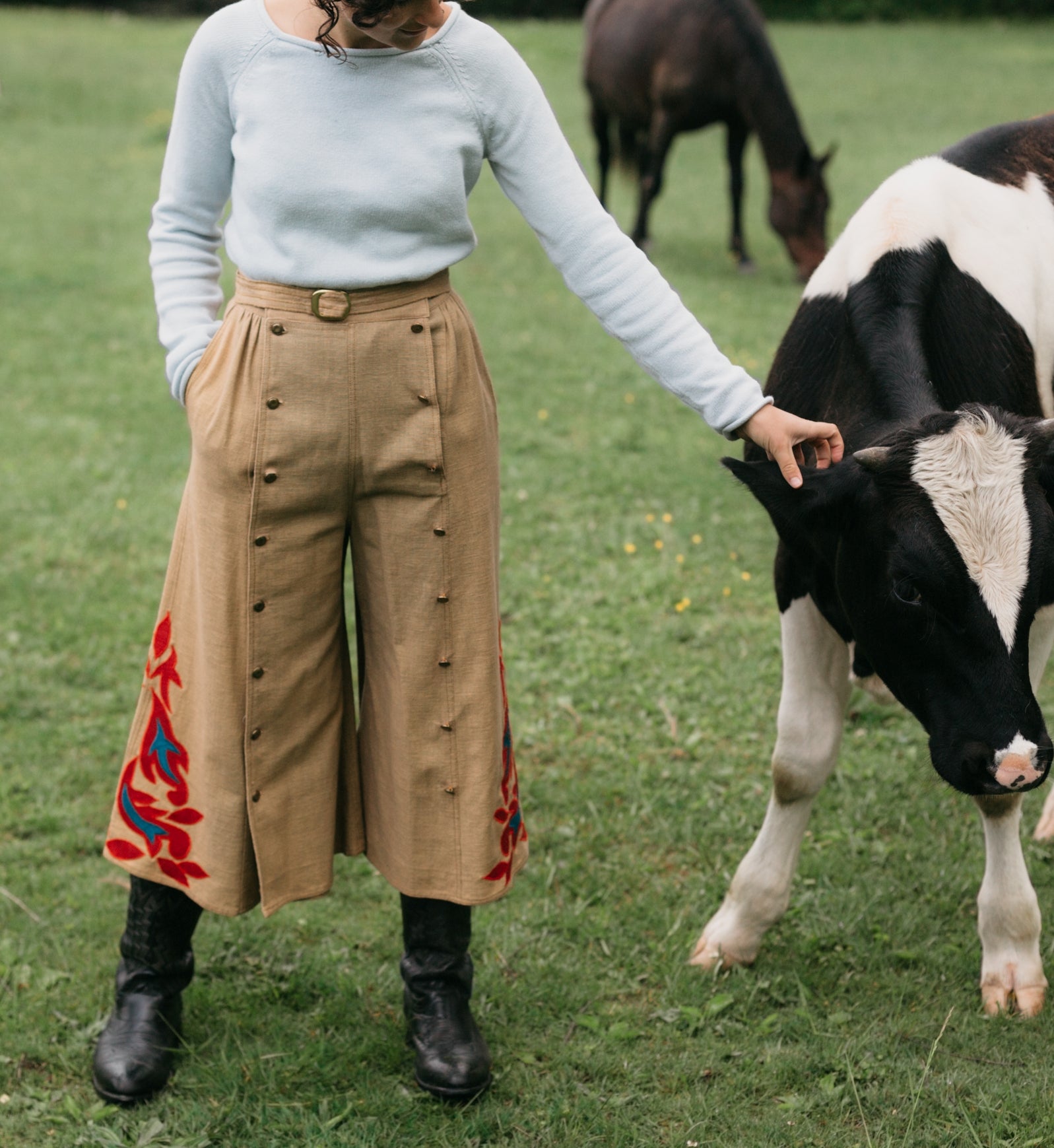 Woman wearing 231 Big Sky Riding Skirt buttoned to the right for a pants effect petting a black and white cow. 