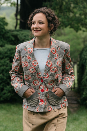 Young Brunette woman smiling surrounded by greenery wearing the 242 Rodeo Cowgirl Jacket with hands in pockets