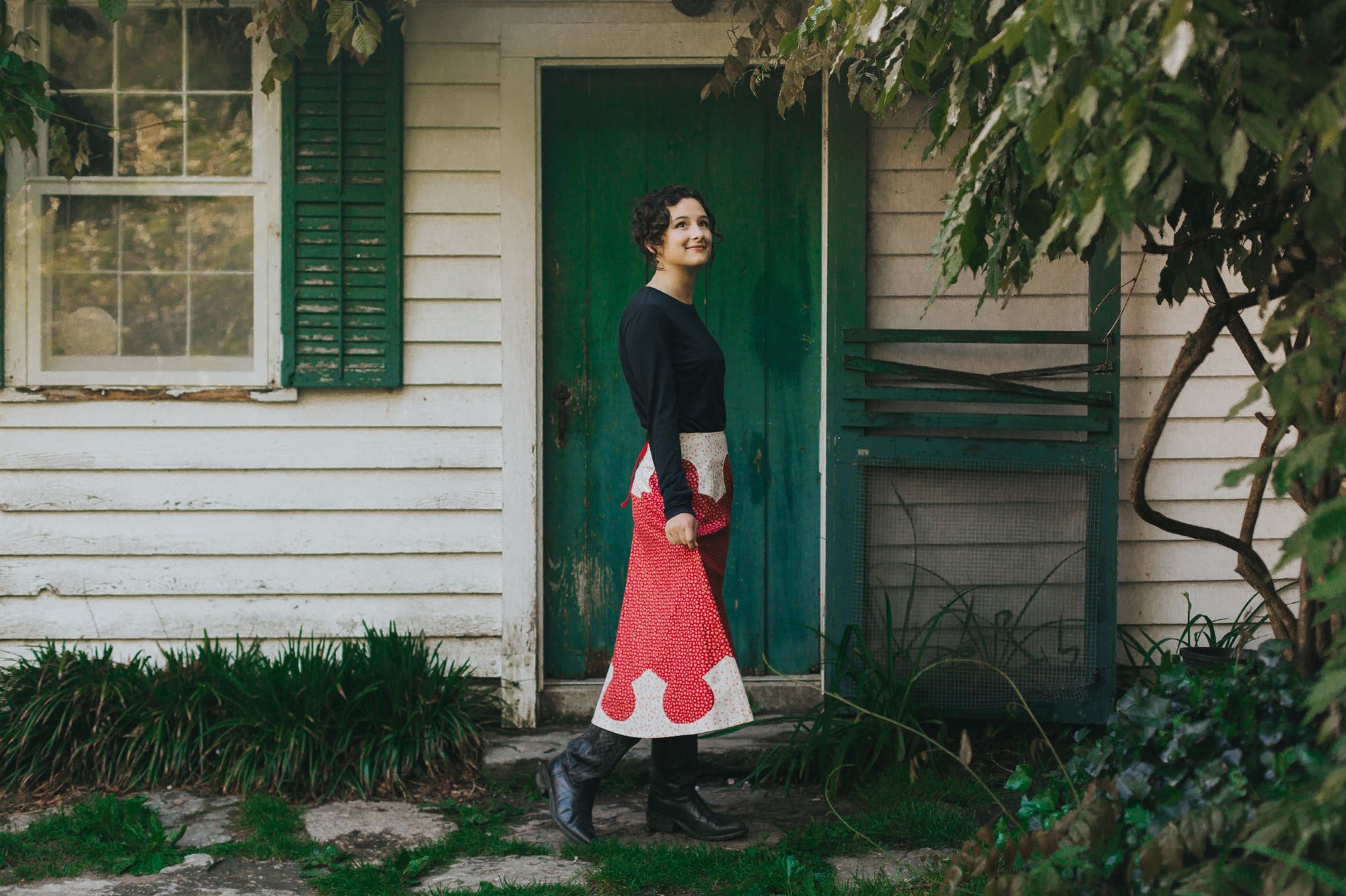 young brunette white woman walking towards the right in front of a house surrounded by greenery wearing 243 Rodeo Cowgirl Skirt