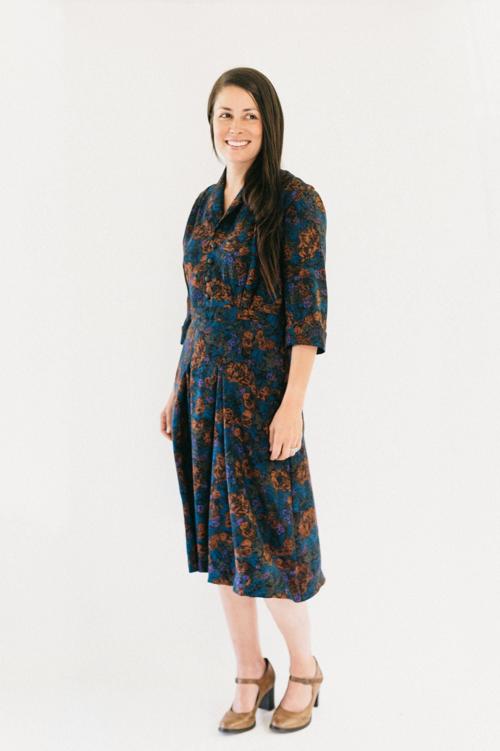 Brunette white women smiling standing slightly turned to the left in front of a white studio backdrop, wearing 247 Lindy Shirtdress, and heels.